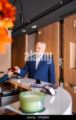 Mature adult businessman checking in at hotel reception desk Stock Photo