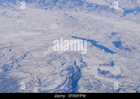 Aerial view of a snow-covered mountain landscape featuring a deep blue reservoir and frozen lakes. Stock Photo