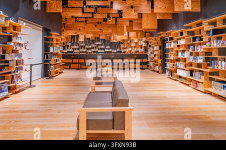 Tokyo, Japan, NOV 22, 2024 - A spacious library interior features rows of wooden bookshelves, a central seating area, and a ceiling covered in suspend Stock Photo