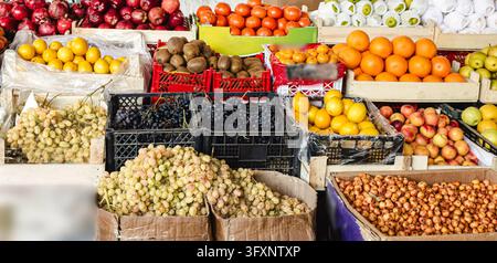 Wide view of red apples, pomegranates, lemons, kiwi, oranges, pears and grapes in crates at an authentic market, real local fruit stall full of fresh Stock Photo