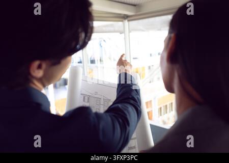 Rear view of Caucasian male and female architects discussing over blueprint in office Stock Photo