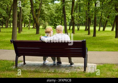 Senior couple embracing on park bench, relaxing together in a lush green park Stock Photo