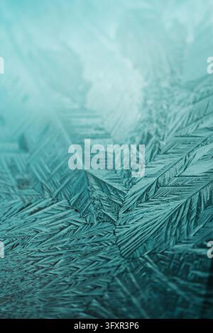 High-quality vertical macro photograph of sharp ice crystals forming a feather-like, geometric frost structure on glass. The teal and cyan gradient wi Stock Photo
