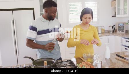 Happy diverse couple cooking and preparing breakfast in kitchen. Spending quality time at home concept. Stock Photo