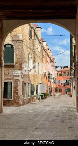 Stone archway frames a narrow street with brick buildings in Venice Stock Photo