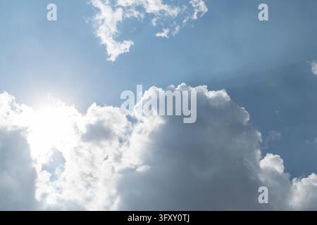 Bright sunlight spills from behind white clouds with dark shaded edges in a vivid blue sky creating a dramatic daytime cloudscape with natural contras Stock Photo