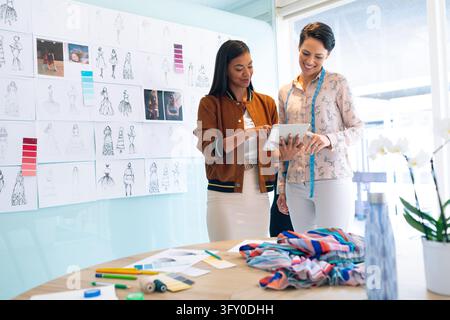 Front view of happy diverse female fashion designers discussing over digital tablet in a modern office Stock Photo