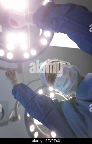 Low angle view of a mature Caucasian female surgeon looking at the camera while moving the surgical lamp to be ready for the operation in clinic Stock Photo