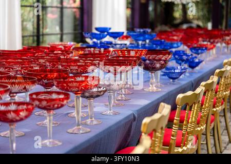 Banquet table with many vintage red and blue crystal glasses, preparations for festive celebrations. Stock Photo