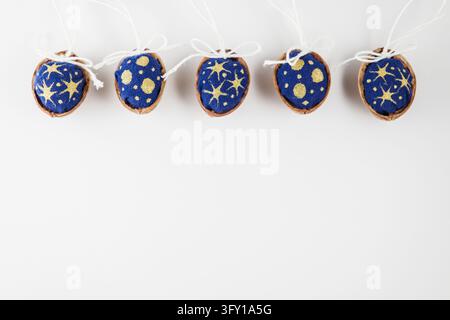 A neat horizontal row of handmade Christmas tree decorations made of walnut shells containing blue fabric with golden star patterns on a white backgro Stock Photo