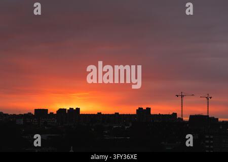 Red and orange sunset behind dark apartment buildings and construction cranes, Netherlands Stock Photo