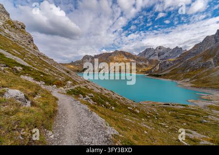 A tranquil hiker explores scenic trails beside a stunning turquoise lake surrounded by rugged alpine peaks under golden fall light Stock Photo