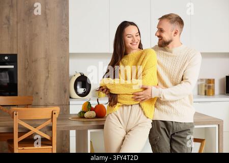Relationship happiness and domestic life, young couple in love embracing in a modern kitchen during autumn season with pumpkins on the wooden table Stock Photo