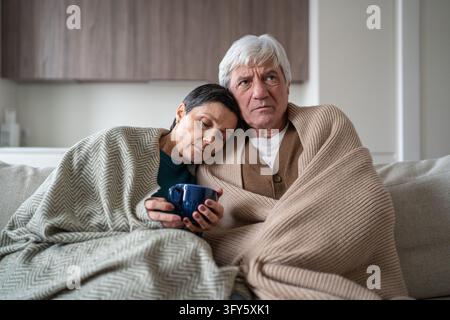 Senior family man and woman sharing cold, sitting together on sofa. Problems with home heating Stock Photo