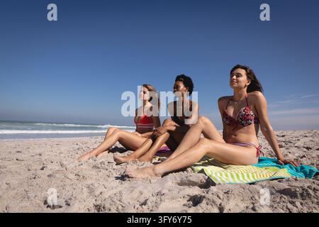 Front view of beautiful young multi ethnic women relaxing on blankets at beach in the sunshine next to the sea Stock Photo