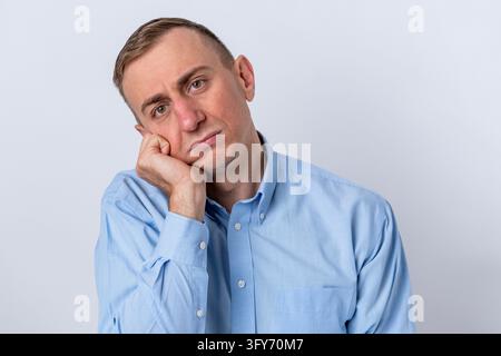 Caucasian man leaning his head on his hand, feeling exhausted and frustrated, portraying concepts of boredom, fatigue, and burnout against a white bac Stock Photo