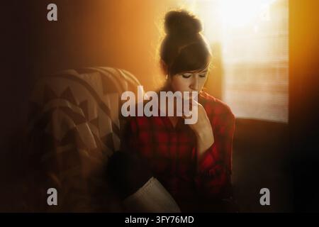 Pensive young woman sitting alone in golden sunlight Stock Photo