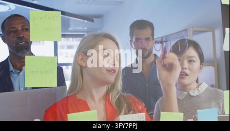 Diverse team collaborates in a bright office. They're engaged in a brainstorming session, using sticky notes for ideas. Stock Photo