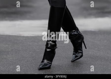 Paris, France - March, 11, 2025: Woman wears black patent leather knee high stiletto boots. Fashion outfit shoes details, street style look accessory, Stock Photo