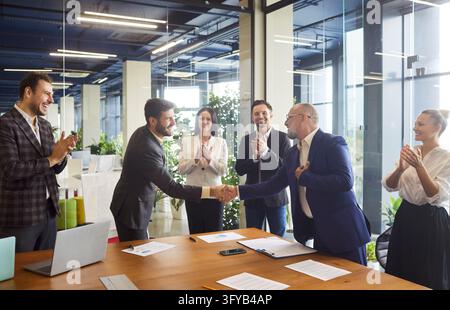 Two confident business partners shake hands, colleagues applaud agreement Stock Photo
