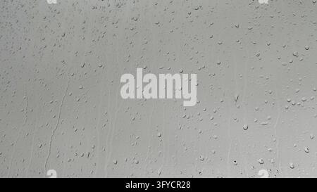 Raindrops on a window pane against an overcast gray sky, rainy day background texture with plenty of copy space. Stock Photo