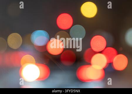 Abstract blurred lights create colorful bokeh circles in red, orange, white and blue against dark evening background. Soft glowing highlights suggest Stock Photo