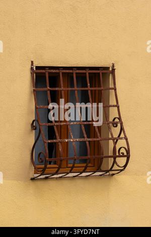 Rusty wrought iron grate on small window in yellow plastered wall Stock Photo