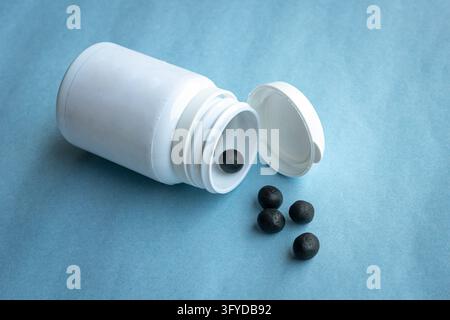 Traditional form of Chinese medicine in small black balls from a bottle. Isolated on blue background. Stock Photo
