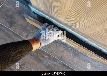 Worker fits a wooden floorboard beside a wall during indoor flooring work Stock Photo