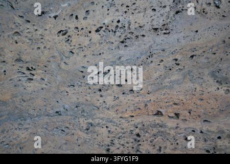 Rough gray and brown pitted surface with irregular cavities forming an abstract textured background. Stock Photo
