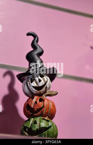 Decorative Halloween figurine featuring three stacked colorful jack-o'-lantern pumpkins wearing a black witch hat against a bright pink background Stock Photo