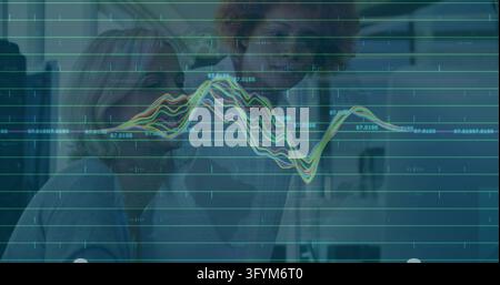Two women wearing white lab coats examining multicolored line graph behind translucent display. Teamwork, collaboration, analytics, research, professi Stock Photo
