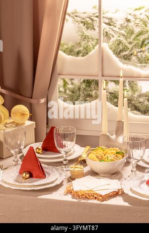 Vertical shot of a festive Christmas Eve table arrangement featuring a bowl of pierogi, lit taper candles, red napkin tree place settings, and beige c Stock Photo