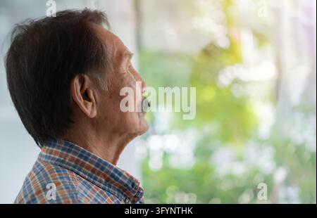 Side view portrait of Asian elderly man wearing striped shirt standing and look outside, copy space Stock Photo