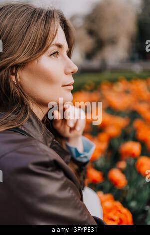 Woman tulip garden profile of a young female in leather jacket looking at orange flowers in a spring park at golden hour Stock Photo