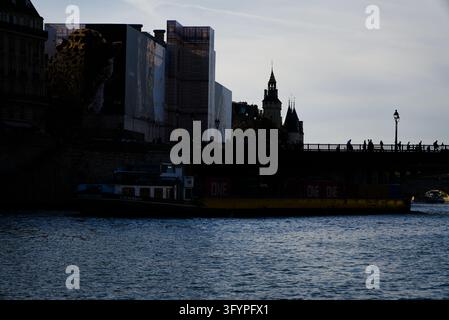Silhouetted view of a cargo barge carrying containers along the Seine River at dusk Stock Photo