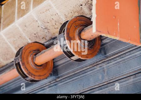 Close up view of a rusty rolling door mechanism, featuring a dusty shaft and orange pulleys, highlighting wear and tear Stock Photo
