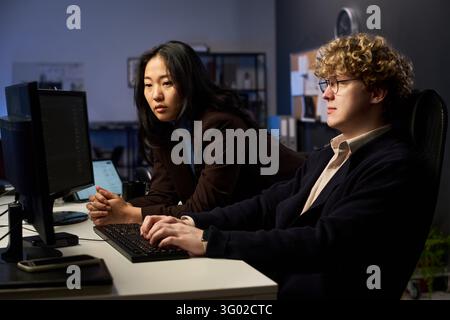 Asian Woman and Man Working on Cybersecurity in Office Stock Photo