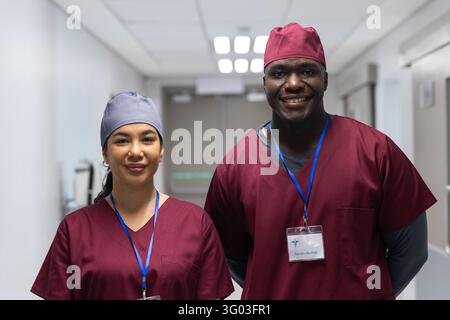 Diverse colleagues standing side by side in hospital corridor wearing maroon scrubs and caps. Healthcare, medical team, professionals, collaboration, Stock Photo