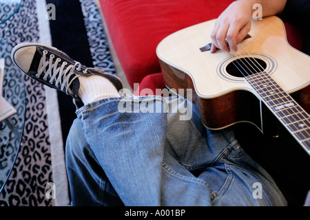 Young male playing an acoustic guitar at home sitting on his couch. Stock Photo