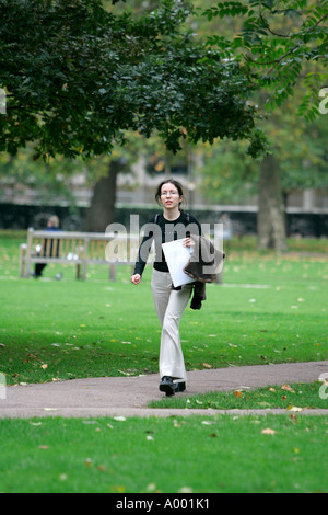 green grass park young smiling lady business dress holding some documents hurry along a path in a park pigeons doves bench happy Stock Photo