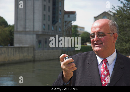 Mature businessman in suit looking at mobile phone with industrial building in the background. Stock Photo