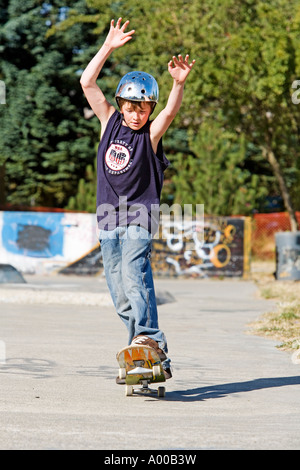 Image of a young boy doing a wheelie on his skate board while using his arms in the air to balance. Stock Photo