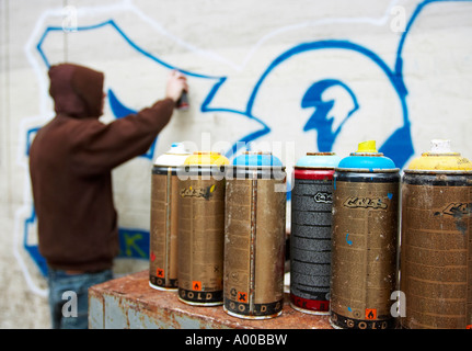 hooded graffiti artist with aerosol cans in foreground Stock Photo