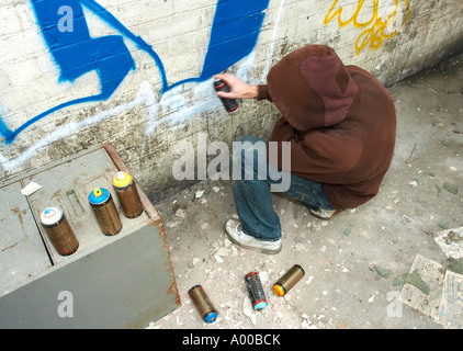 hooded graffiti artist crouching & spraying Stock Photo