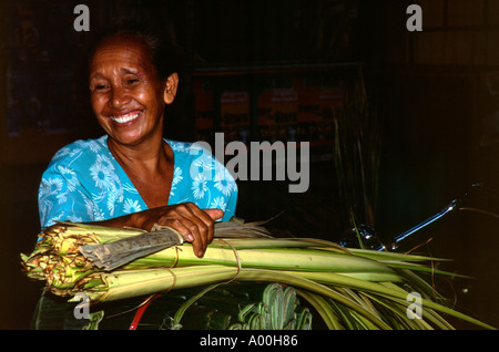 laughing local woman with large bundle of reeds for sale as roofing material near kuta bali indonesia Stock Photo