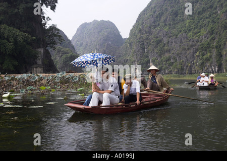 Visitors on boat trip to Tam Coc caves with foot rowing boatman Ngo Dong River near Ninh Binh north Vietnam Stock Photo