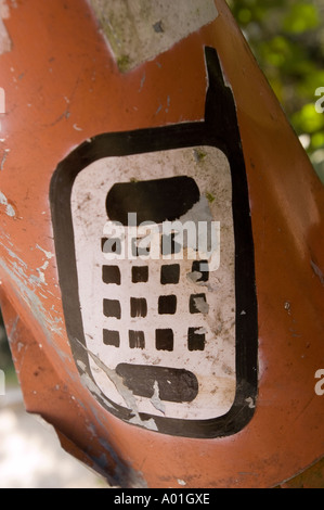 Old crushed sign with mobile phone painting in Sikkim, India. Close-up of weathered orange metal with a vintage cell phone icon and keypad. Stock Photo