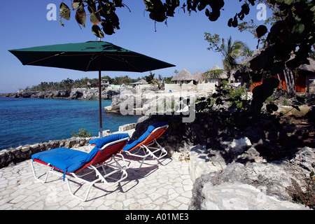 Chaise lounge and beach umbrella on a stone terrace overlooking an azur sea, Negril, Jamaica Stock Photo