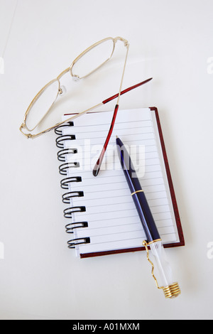 Blue and gold pen with glowing light, on black spiral hard cover notebook and reading glasses Stock Photo